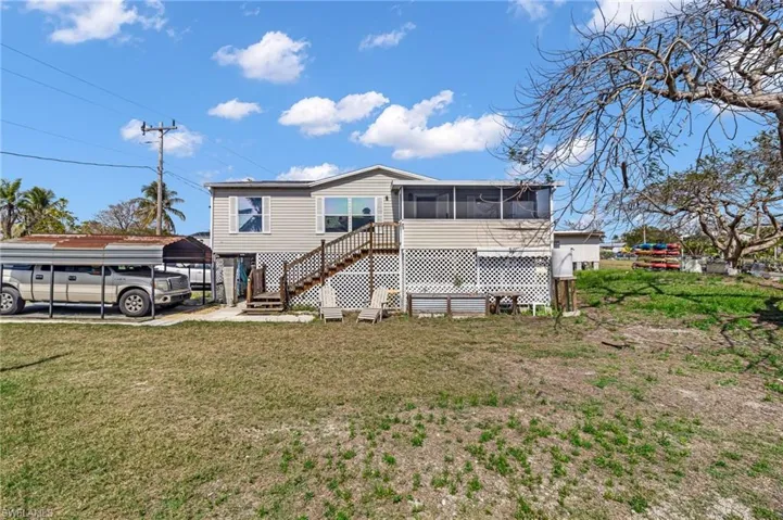 Back of property featuring stairs, a detached carport, a lawn, and a sunroom