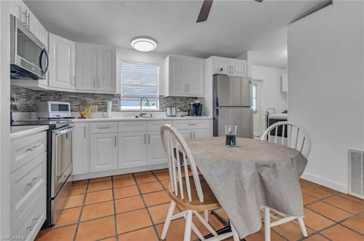 Kitchen featuring tasteful backsplash, white cabinets, stainless steel appliances, light countertops, and a sink