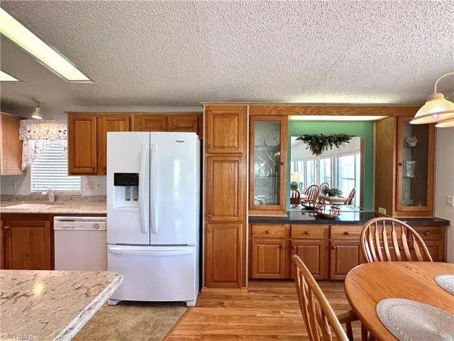 Kitchen with a textured ceiling, light hardwood / wood-style flooring, light stone counters, dishwashing machine, and white refrigerator with ice dispenser