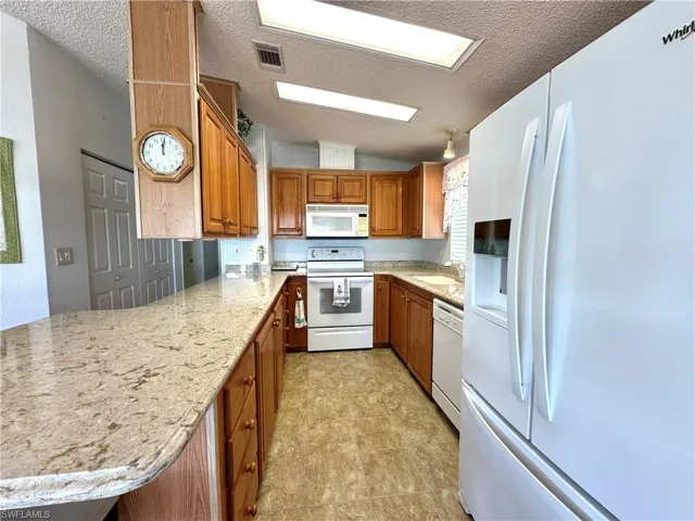 Kitchen featuring light stone counters, white appliances, a textured ceiling, and light tile floors