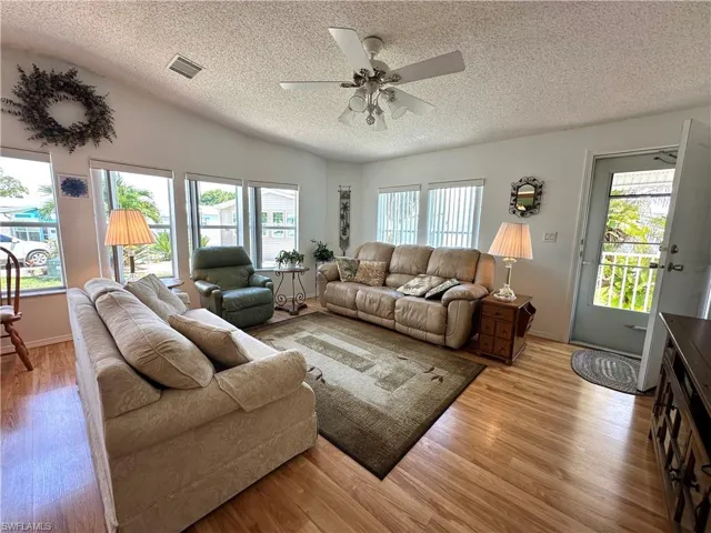 Living room featuring a textured ceiling, light wood-type flooring, vaulted ceiling, and ceiling fan