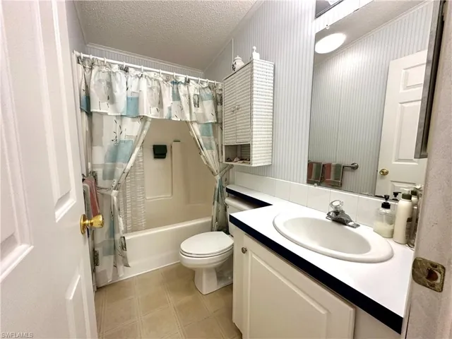 Full bathroom with a textured ceiling, tile flooring, shower / bath combo with shower curtain, oversized vanity, and toilet