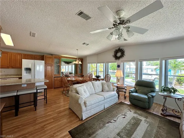 Living room with a textured ceiling, light wood-type flooring, and ceiling fan