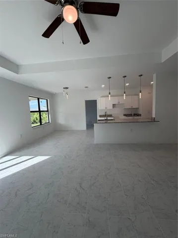 Open-concept interior featuring light-toned tile flooring, tray ceilings, recessed lighting, white cabinetry, and a breakfast bar with stone-finish countertops