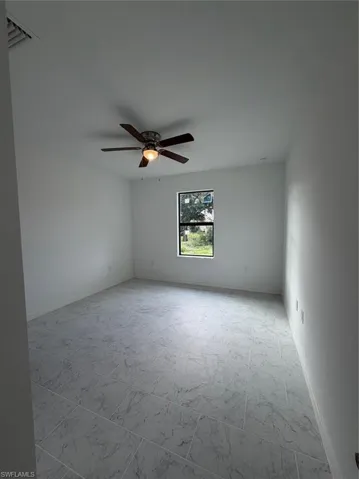 Neutral interior featuring stone-patterned tile flooring, a dark-framed window, and a ceiling fan with integrated lighting