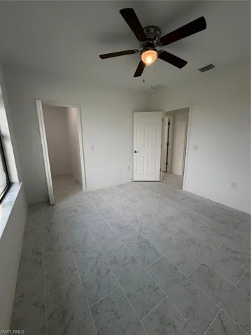 Neutral-toned interior featuring large-format tile flooring with a veined pattern, six-panel interior doors, and a ceiling-mounted fan with integrated lighting