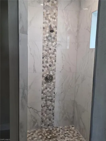Walk-in shower featuring large-format porcelain tile walls, a central vertical mosaic pebble accent, matching pebble flooring, and a chrome shower fixture