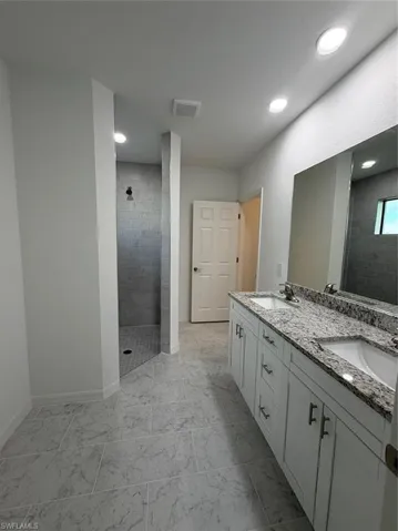 Dual-sink vanity with stone-finish countertop, full-width mirror, tile flooring, and walk-in shower with tiled surround