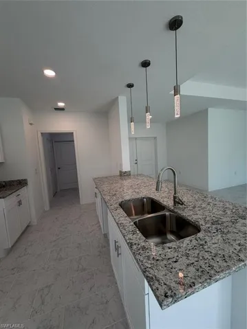 Kitchen island featuring stone countertops, a dual-basin stainless steel sink with an arched faucet, and three contemporary cylindrical pendant lights