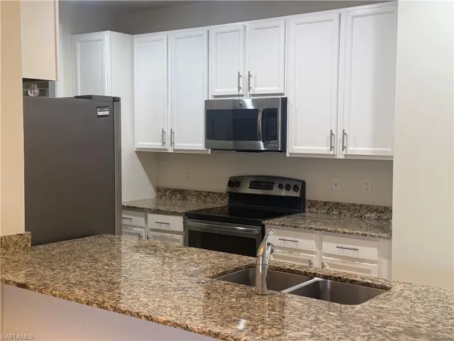 Kitchen featuring stainless steel appliances, dark stone countertops, and white cabinetry