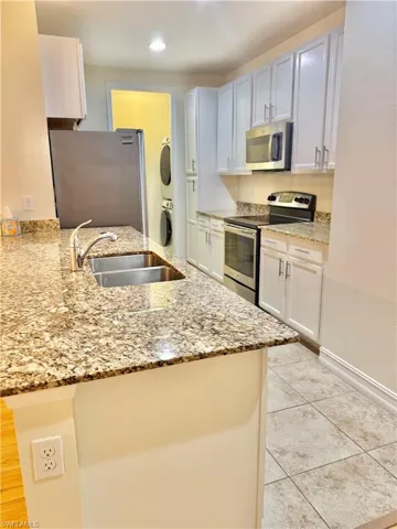 Kitchen with stainless steel appliances, light stone countertops, white cabinetry, stacked washing machine and dryer, and recessed lighting