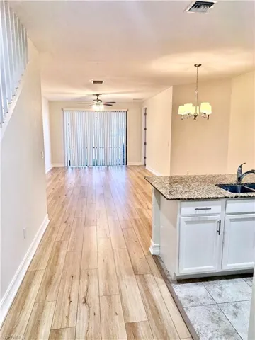 Kitchen with white cabinets, light wood-type flooring, light stone countertops, open floor plan, and ceiling fan