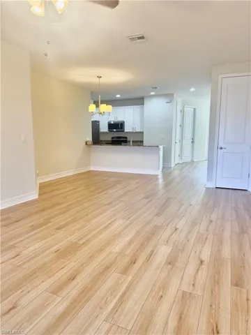 Unfurnished living room featuring ceiling fan, light wood-style floors, and a chandelier