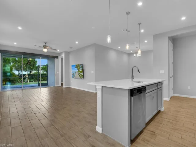 Kitchen with an island with sink, stainless steel dishwasher, pendant lighting, light hardwood / wood-style floors, and sink