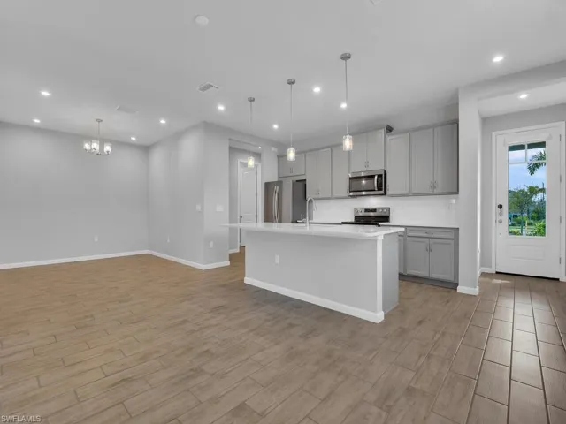 Kitchen featuring gray cabinetry, stainless steel appliances, pendant lighting, and a kitchen island with sink