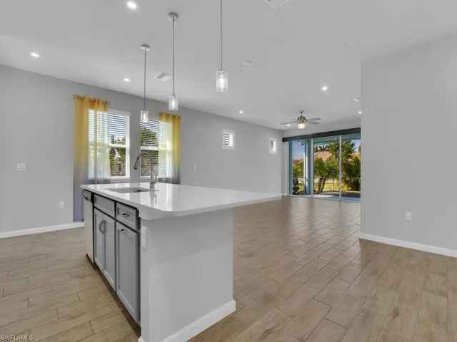 Kitchen with sink, an island with sink, light tile flooring, and decorative light fixtures