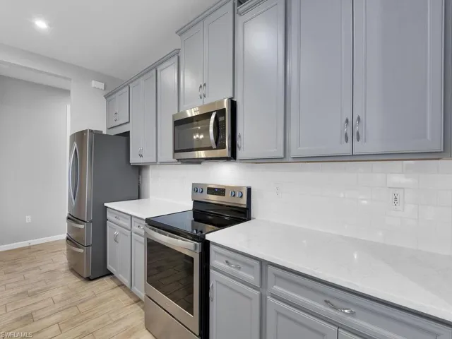 Kitchen with light tile flooring, gray cabinetry, backsplash, light stone countertops, and appliances with stainless steel finishes