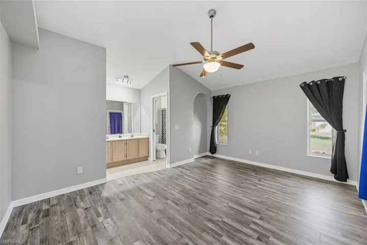 Unfurnished bedroom with vaulted ceiling, light wood-style flooring, ensuite bathroom, and ceiling fan