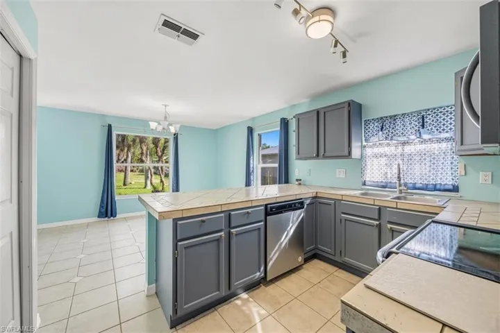 Kitchen featuring tile countertops, gray cabinetry, a peninsula, and light tile patterned floors