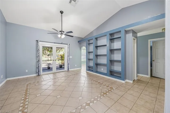 Empty room featuring light tile patterned floors, built in shelves, vaulted ceiling, ceiling fan, and french doors