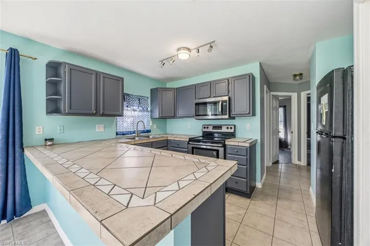 Kitchen featuring tile counters, open shelves, stainless steel appliances, light tile patterned floors, and a peninsula