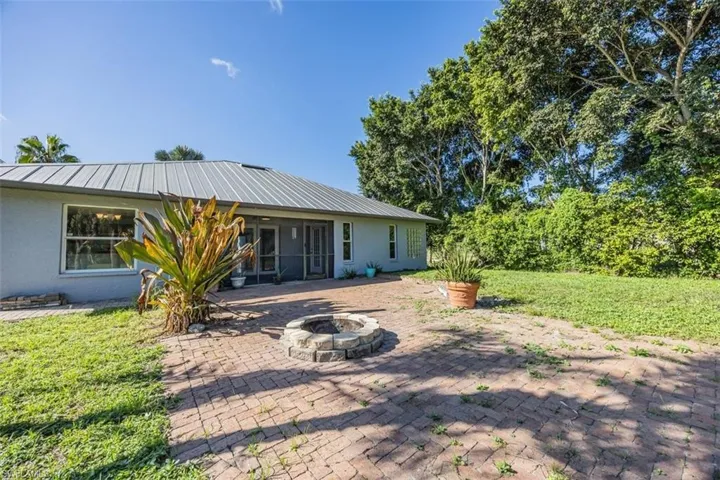 Rear view of property featuring a lawn, a sunroom, a patio area, and a fire pit