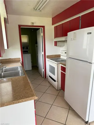 Kitchen with sink, light tile patterned flooring, and white appliances