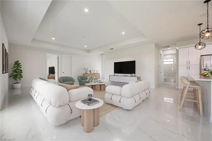Living room with a raised ceiling, recessed lighting, visible vents, and marble finish floor