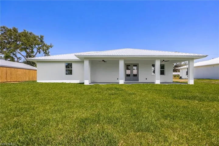 Rear view of house featuring metal roof, a lawn, a ceiling fan, and stucco siding