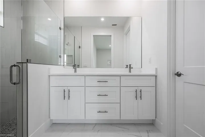 Bathroom with marble finish floor, double vanity, a shower stall, and baseboards