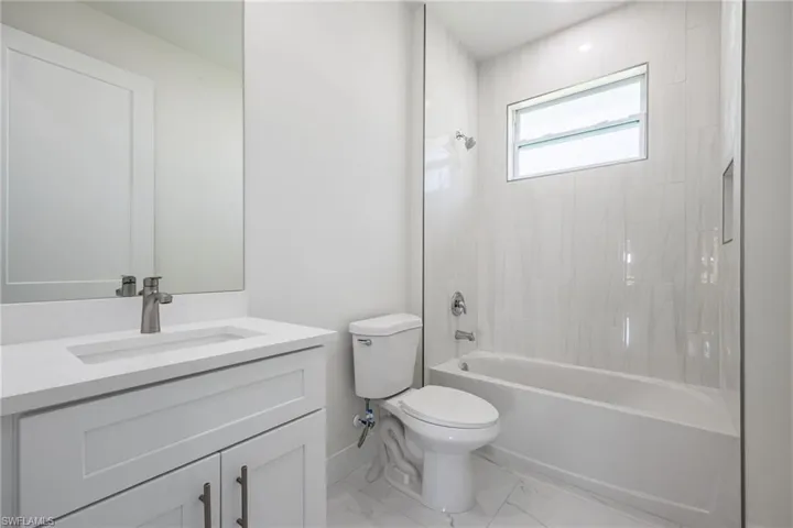 Full bath with marble finish floor, toilet, shower / bath combination, vanity, and baseboards