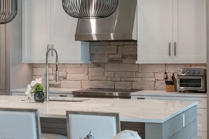 Kitchen featuring wall chimney exhaust hood, decorative backsplash, and white cabinets