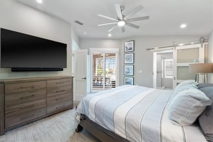 Bedroom with a barn door, recessed lighting, a ceiling fan, vaulted ceiling, and connected bathroom