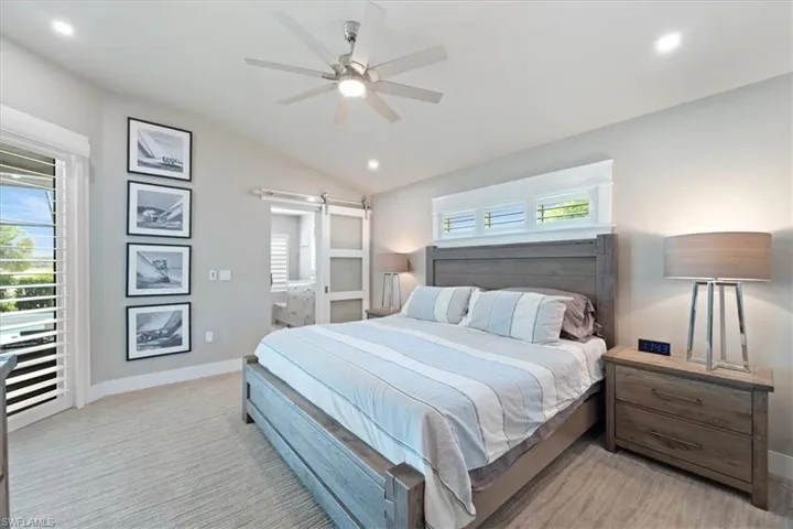 Bedroom with a barn door, lofted ceiling, recessed lighting, light colored carpet, and ensuite bathroom