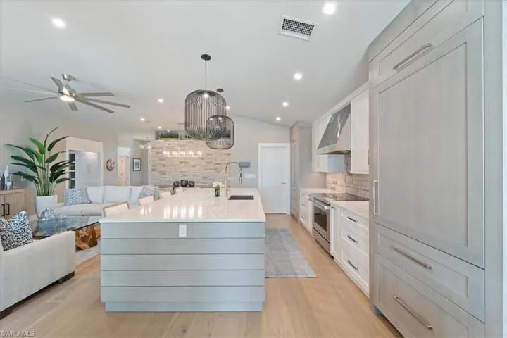 Kitchen with stainless steel electric range oven, wall chimney range hood, open floor plan, decorative backsplash, and a kitchen island with sink