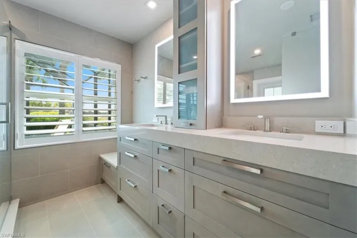 Bathroom with double vanity, a tile shower, tile patterned flooring, and tile walls