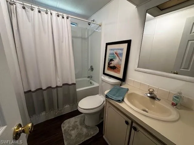 Full bathroom featuring shower / bath combo with shower curtain, oversized vanity, toilet, and hardwood / wood-style floors