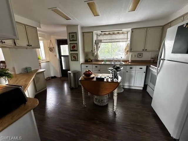 Kitchen with dark wood-type flooring, sink, white appliances, and a textured ceiling