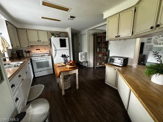 Kitchen with wood counters, dark hardwood / wood-style floors, sink, white appliances, and a textured ceiling