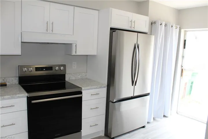 Kitchen with custom range hood, appliances with stainless steel finishes, light hardwood / wood-style flooring, light stone counters, and white cabinets