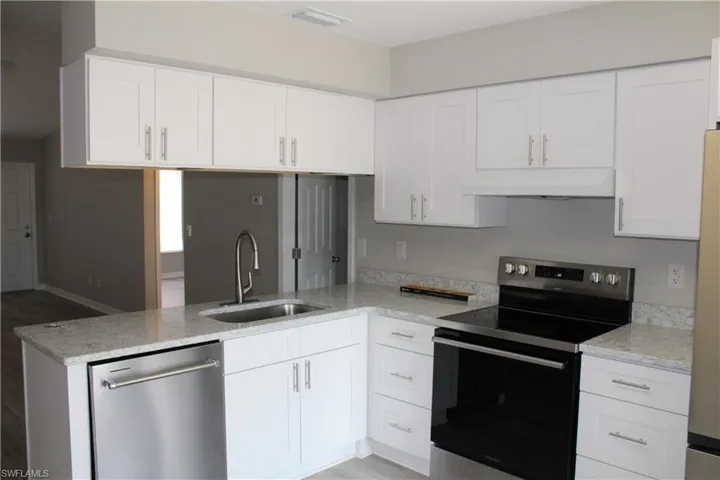 Kitchen with white cabinetry, appliances with stainless steel finishes, light stone counters, and custom range hood
