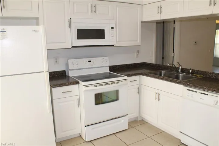 Kitchen with white cabinetry, sink, light tile patterned floors, and white appliances