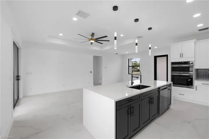 Kitchen featuring a raised ceiling, light marble finish floors, open floor plan, white cabinetry, and recessed lighting