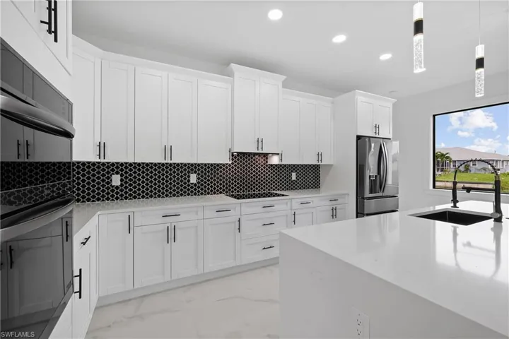 Kitchen featuring light stone counters, appliances with stainless steel finishes, hanging light fixtures, light marble finish flooring, and decorative backsplash