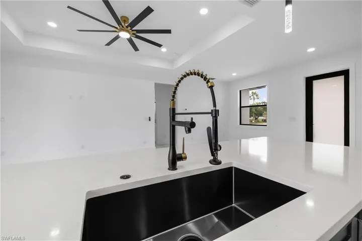 Kitchen view of a raised ceiling, light stone counters, recessed lighting, and a ceiling fan