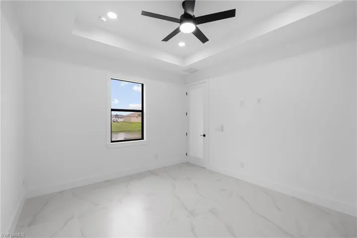 Spare room featuring a tray ceiling, recessed lighting, light marble finish flooring, and ceiling fan