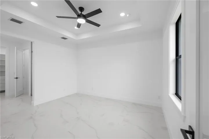 Unfurnished bedroom with a raised ceiling, light marble finish floors, a ceiling fan, and recessed lighting