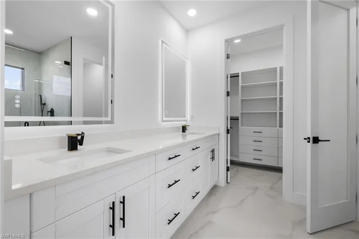 Full bathroom featuring a stall shower, double vanity, light marble finish flooring, recessed lighting, and a spacious closet