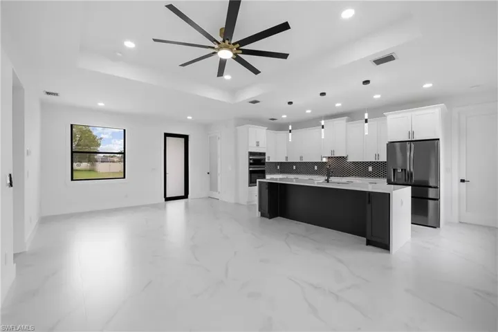 Kitchen featuring a tray ceiling, open floor plan, stainless steel appliances, white cabinetry, and a kitchen island with sink