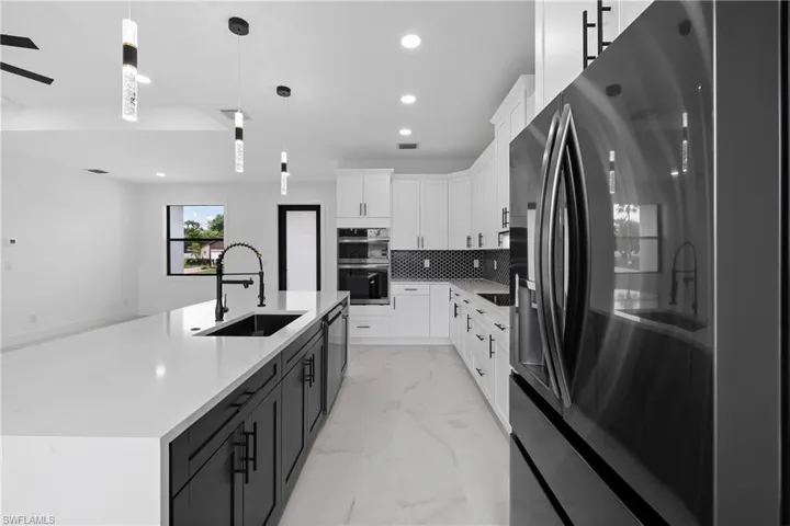 Kitchen with appliances with stainless steel finishes, white cabinets, light marble finish floors, decorative light fixtures, and light stone countertops